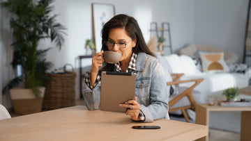 Woman drinking a coffee and comfortably reading from her iPad tablet using ThinOptics reading glasses, demonstrating the our focus on clarity and convenience for digital device users.