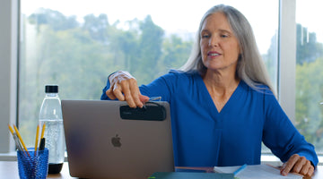 Woman reaching for her ThinOptics Reading Glasses from the back of her laptop