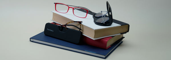 ThinOptics Full Frame Reading Glasses with Cases on a stack of books against a white backdrop