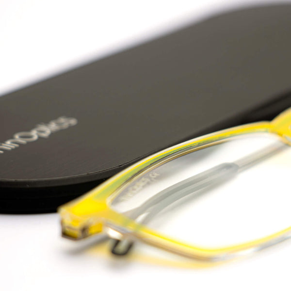 ThinOptics reading glasses and a sleek black case: minimalist design with thin lenses. The compact, brushed metal case offers a modern, portable solution for individuals needing reading glasses.