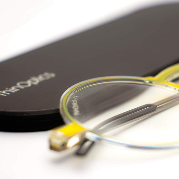 ThinOptics reading glasses and a sleek black case: minimalist design with thin and round lenses. The compact, brushed metal case offers a modern, portable solution for individuals needing reading glasses.