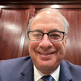 Smiling man with glasses in a blue suit and tie.