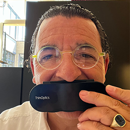 Man smiles while holding a ThinOptics reading glasses case in front of his mouth.