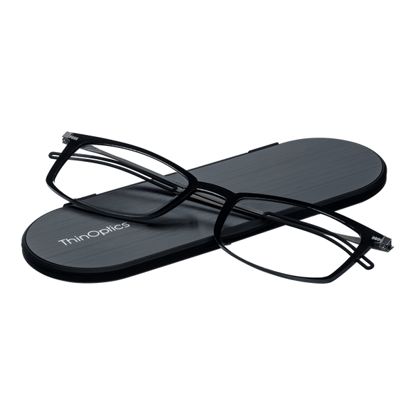 Black ThinOptics reading glasses rest unfolded on their sleek, brushed-metal carrying case.