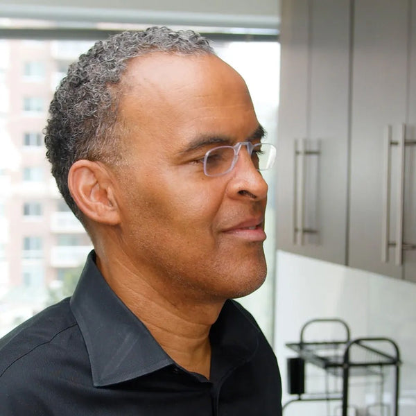 A man wearing rimless glasses turns his head to the right in profile.