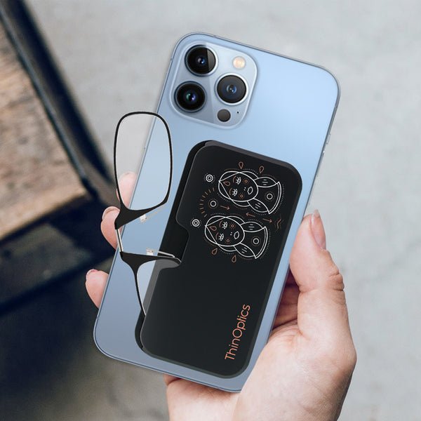 Hand holds a blue smartphone with a ThinOptics reading glasses case attached to the back. The black case features a minimalist design.