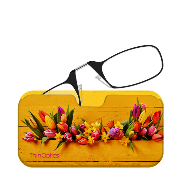 Black reading glasses rest on a vibrant yellow floral glasses case. Colorful tulips and daffodils are arranged on the case.