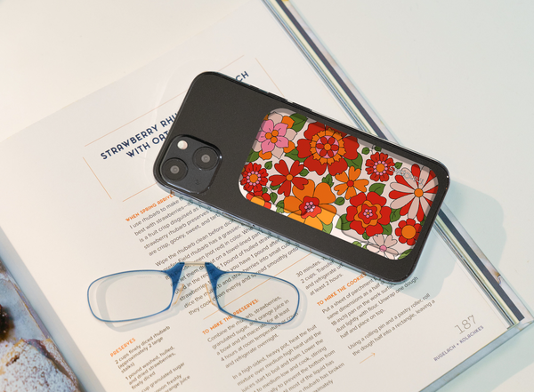 Black iPhone case with a retro floral pattern of red, orange, and white flowers laid on an open cookbook.