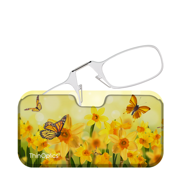 Silver ThinOptics reading glasses folded atop a floral patterned case featuring yellow daffodils and monarch butterflies.