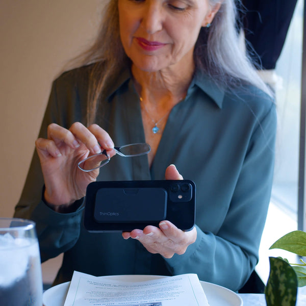Woman holds ThinOptics reading glasses and uses them to read a menu on her phone.