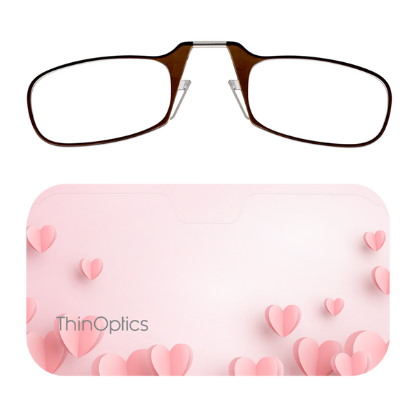 Brown ThinOptics reading glasses folded on top of a pink heart-patterned case.