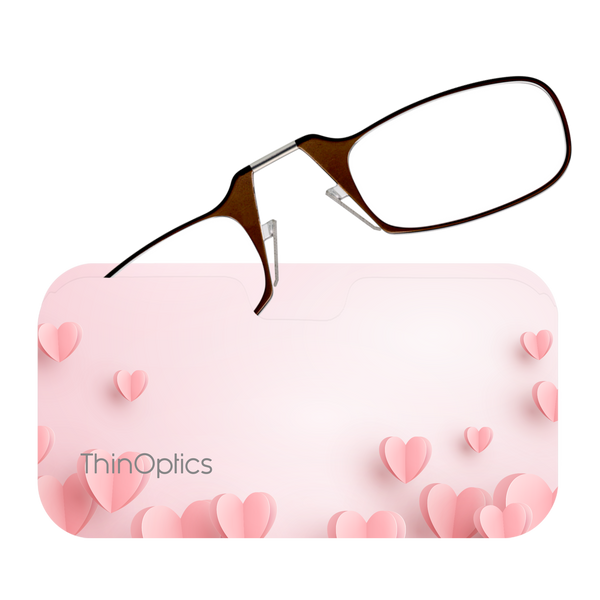 Brown ThinOptics reading glasses rest on a pink heart-patterned case.