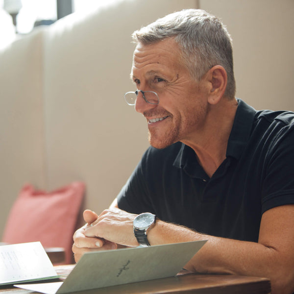 Smiling man with short gray hair and glasses reviews a menu at a restaurant table.