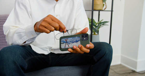 Man removes ThinOptics reading glasses from a green phone case with a snowy mountain landscape.
