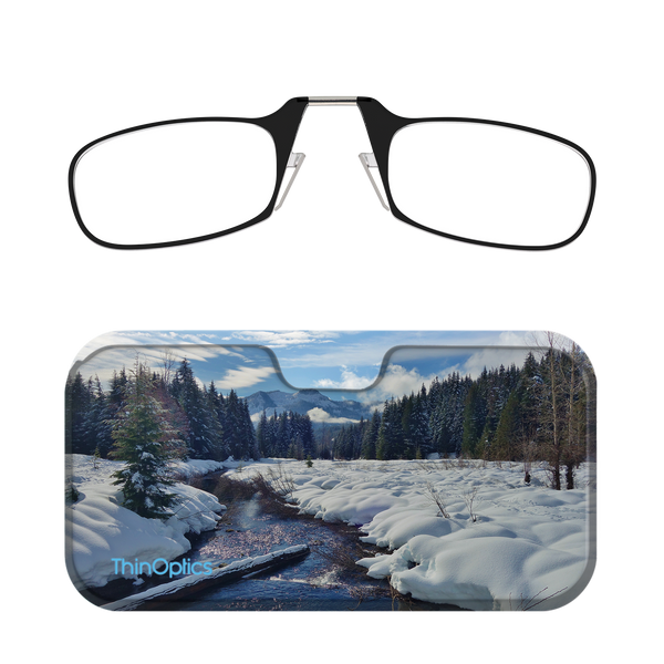 Black ThinOptics reading glasses rest on a scenic landscape case featuring a snow covered forest and stream.