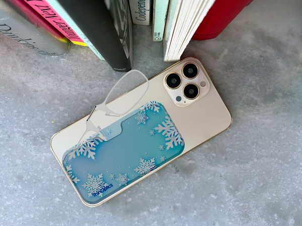 A pair of ThinOptics reading glasses rest on a snowflake-patterned phone case adhered to the back of a smartphone.