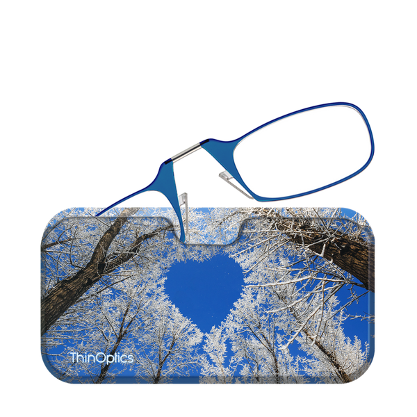 Blue ThinOptics reading glasses rest on a patterned case featuring snow-covered trees against a clear blue sky.