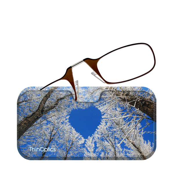 Brown folding reading glasses rest on a blue ThinOptics case featuring a wintery scene of snow-covered trees against a bright blue sky.