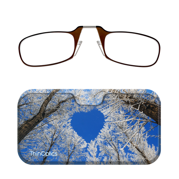 Brown ThinOptics reading glasses folded on a slim case featuring a photo of snow-covered trees against a blue sky.