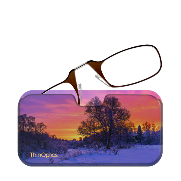 Brown ThinOptics reading glasses rest on a slim case featuring a vibrant winter sunset over a snow-covered landscape.