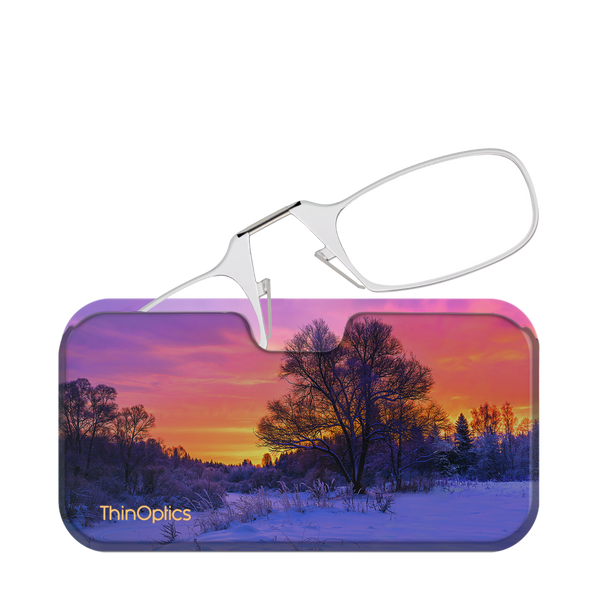 ThinOptics reading glasses rest unfolded atop a slim case featuring a scenic winter sunset.