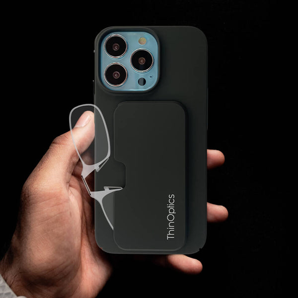 Hand holds a slim, black phone case with integrated ThinOptics reading glasses against a dark background.
