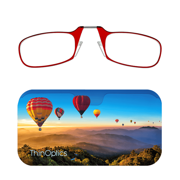 Red ThinOptics reading glasses rest atop a slim case featuring hot air balloons soaring over a misty mountain valley.