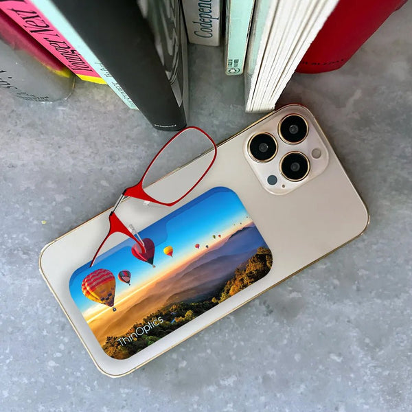 ThinOptics reading glasses with vibrant hot air balloon printed case rest on a smartphone.