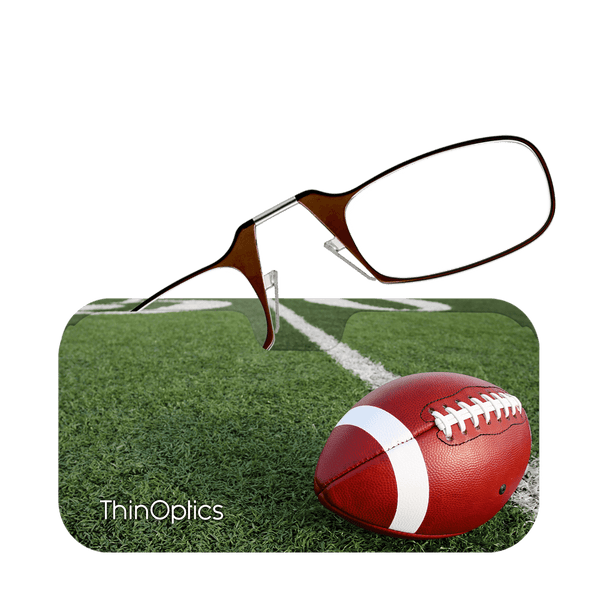 Brown ThinOptics reading glasses rest on a football positioned on a football field.