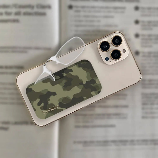 Camouflage ThinOptics reading glasses rest on a smartphone, demonstrating the product's portability and sleek design.