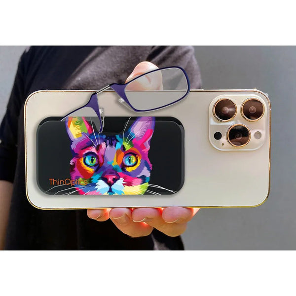 Hand holds a gold smartphone with a ThinOptics case featuring a colorful, abstract cat design. A pair of ThinOptics reading glasses rests on top.