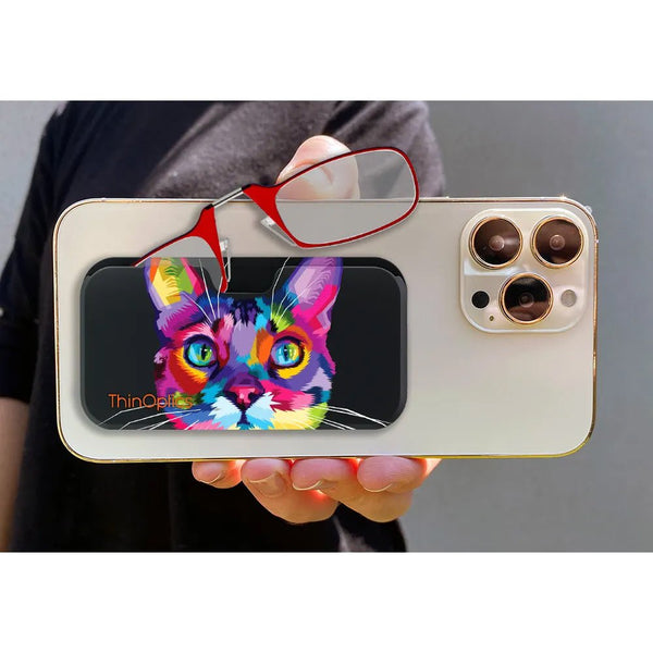 Hand holds up a smartphone with a ThinOptics case featuring a vibrant, colorful cat design. A pair of red ThinOptics reading glasses are folded and resting on the top of the case.