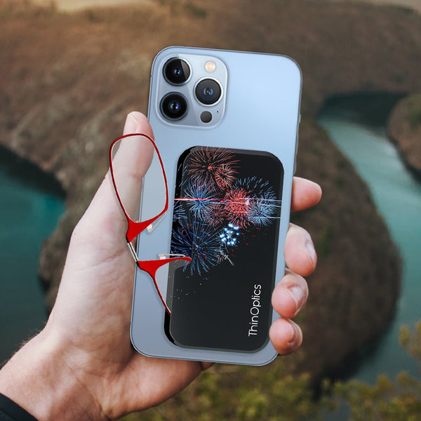 Hand holds a smartphone with a ThinOptics case and a pair of red reading glasses attached, showcasing the product's convenience and sleek design.