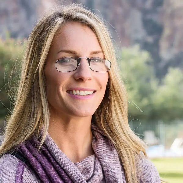 Woman with blonde hair and rectangular glasses smiles outdoors.