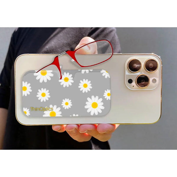 Hand holds a smartphone with ThinOptics readers attached to a gray daisy-patterned case.