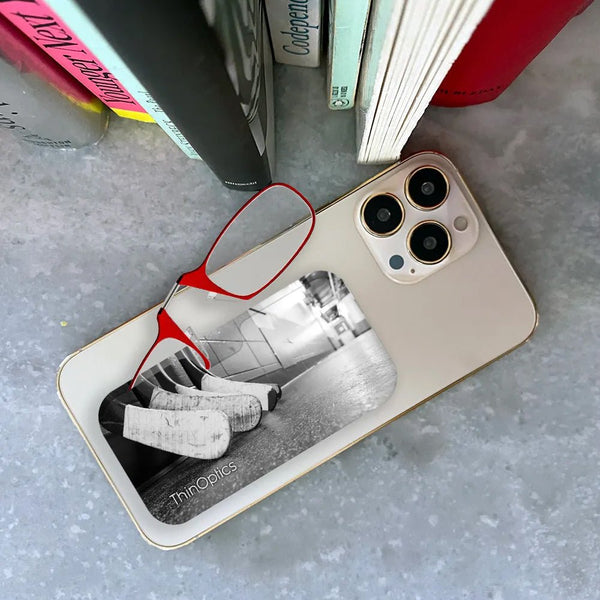 ThinOptics reading glasses attached to the back of a smartphone with a black and white photo of hockey sticks in a locker room.