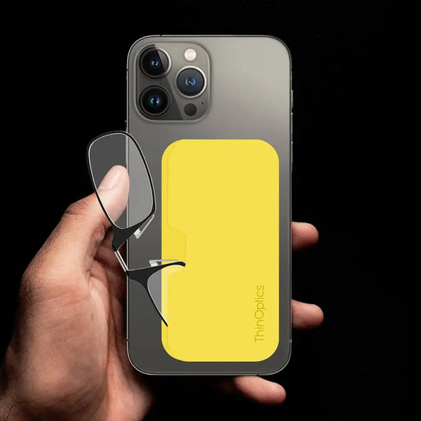 Hand holding a smartphone with a bright yellow ThinOptics case that holds a pair of reading glasses.