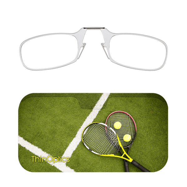 Silver ThinOptics reading glasses folded atop a green tennis court with two rackets and tennis balls.