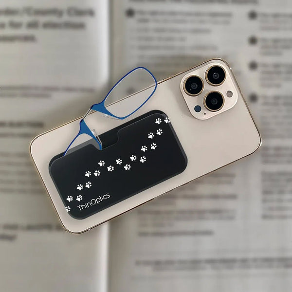 ThinOptics blue reading glasses rest on a black paw-print phone case attached to a smartphone screen.