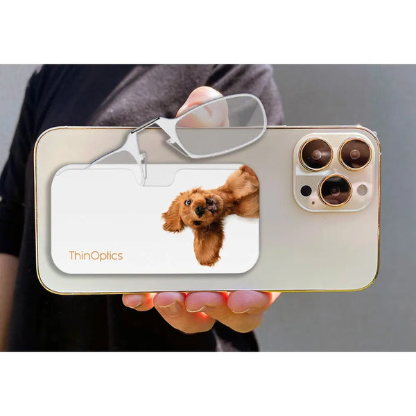 Person holds ThinOptics reading glasses and case attached to back of phone featuring a brown cocker spaniel puppy.