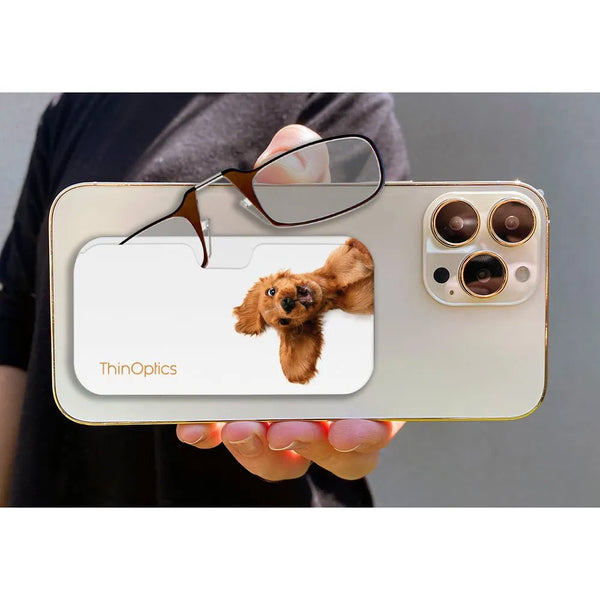 Hand holds smartphone with ThinOptics reading glasses tucked into a slim case featuring a cute brown dog peeking over the edge.
