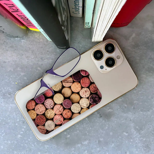 ThinOptics readers rest on a smartphone with a wine cork pattern case displayed on a table.