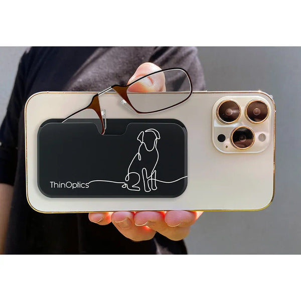 Hand holds ThinOptics reading glasses attached to sleek black phone case with minimalist dog design.