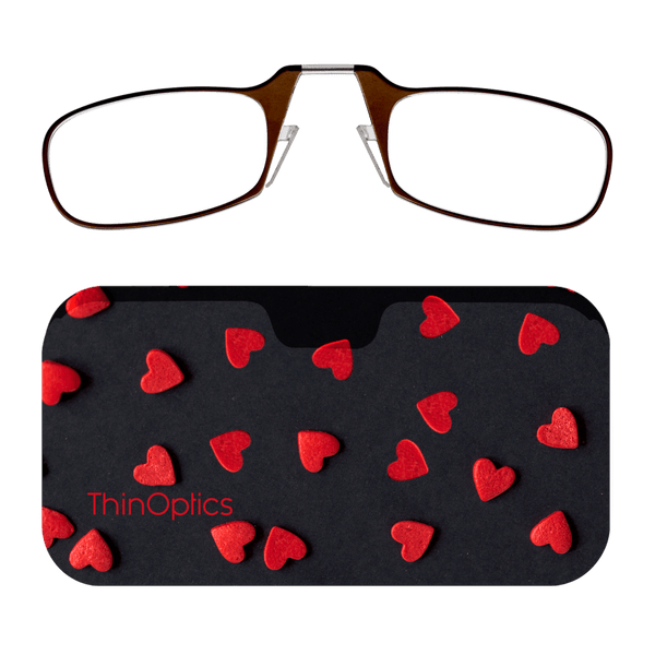 Brown ThinOptics reading glasses rest atop a black heart-patterned carrying case.