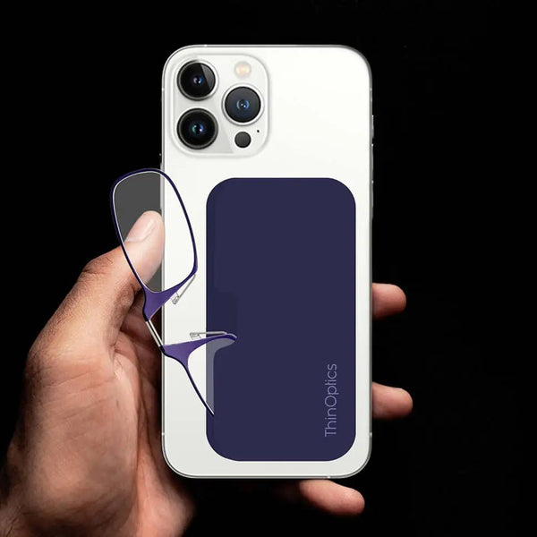 Hand holds a white smartphone with a navy ThinOptics case and a pair of slim reading glasses.