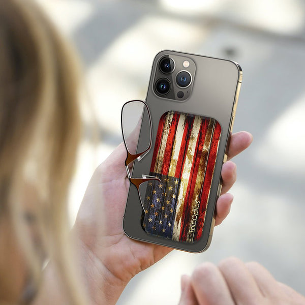 Woman holds smartphone with attached ThinOptics reading glasses. The glasses case features a rustic American flag design.