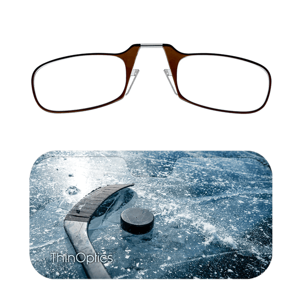 Brown ThinOptics reading glasses displayed above a hockey puck and stick resting on an icy surface.