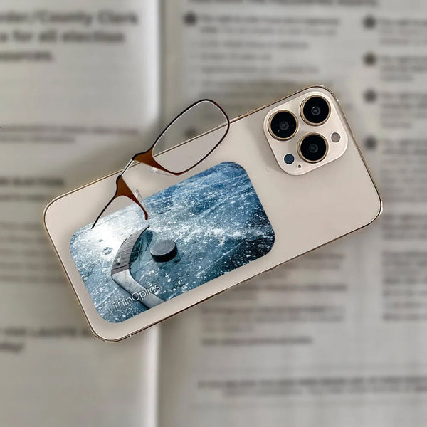 ThinOptics reading glasses rest on a smartphone displaying a hockey puck on an icy surface.
