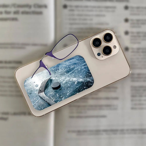 Purple ThinOptics reading glasses rest on a smartphone displaying a hockey puck on an icy surface.