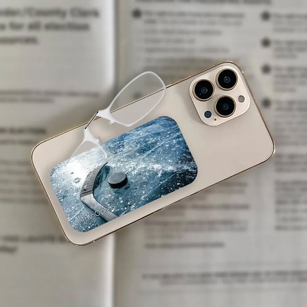 ThinOptics reading glasses rest on a gold smartphone displaying a hockey puck on ice.